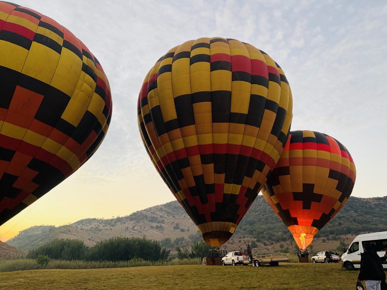 Three balloons glowing at dawn with the burner flame and mountains behind