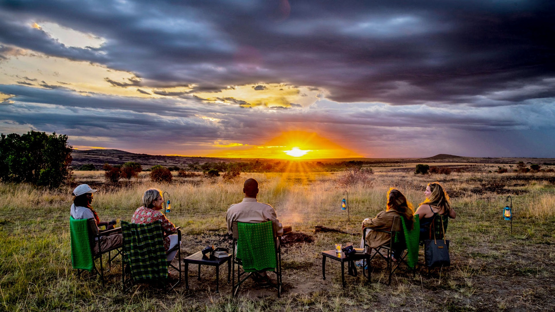 A diverse group of people sharing a sundowner together at sunset in the African savanna