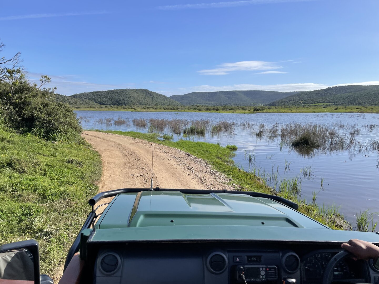 The view from the Kariega game-drive vehicle — a dirt track winding past a tranquil lake with green hills in the distance