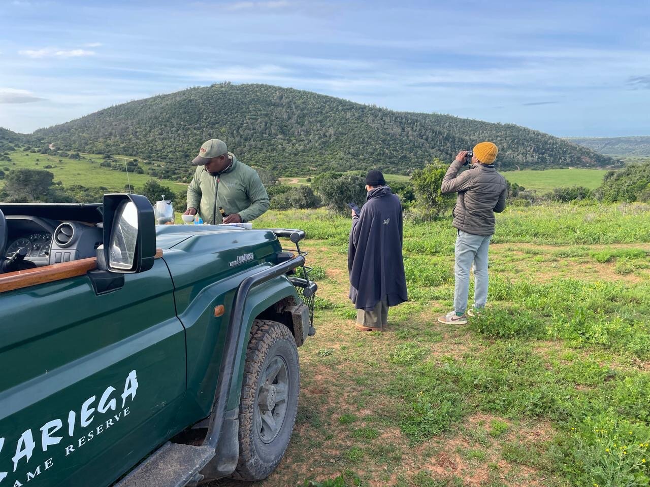 The green Kariega Game Reserve Land Cruiser parked on a rise, our ranger setting up sundowner drinks on the bonnet while we take in the rolling hills