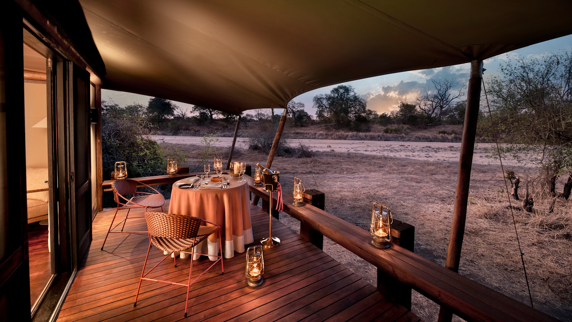A romantic private dinner on the deck of a luxury safari lodge at golden hour