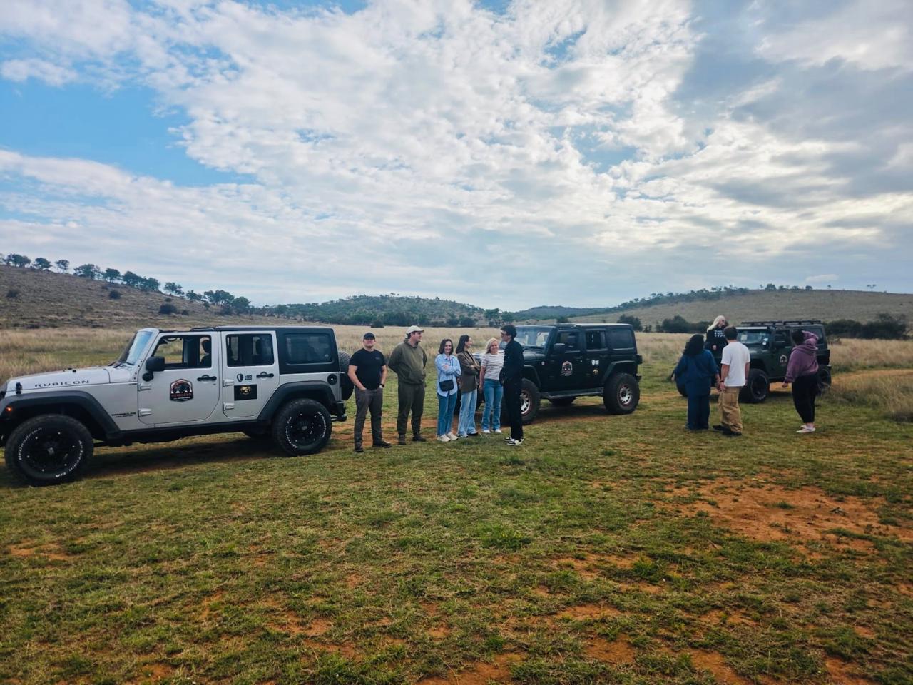 A fleet of safari jeeps and a group of guests gathering between vehicles at the Lion and Safari Park