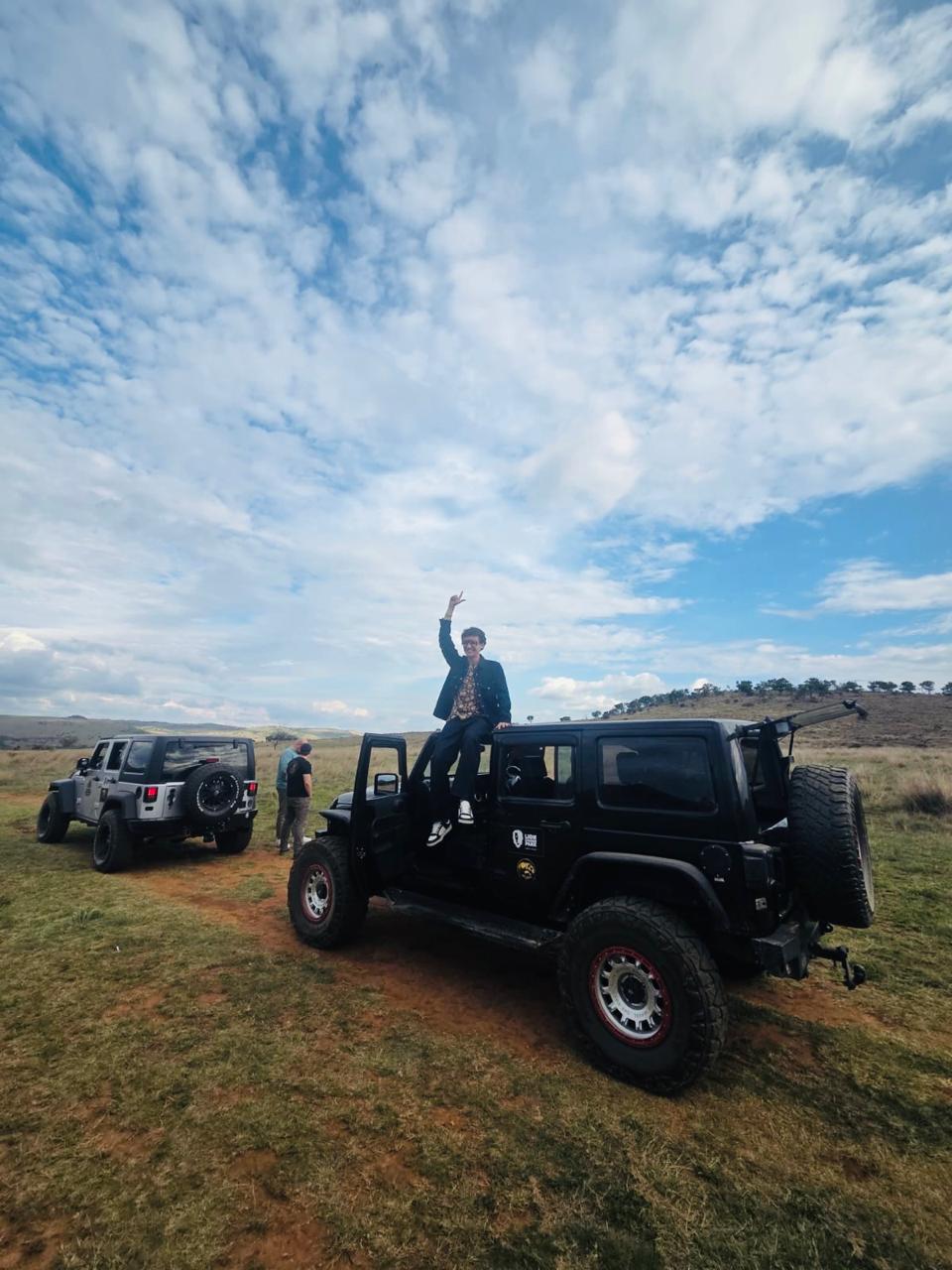 A guest sitting on top of a safari jeep with dramatic clouds and rolling bushveld behind