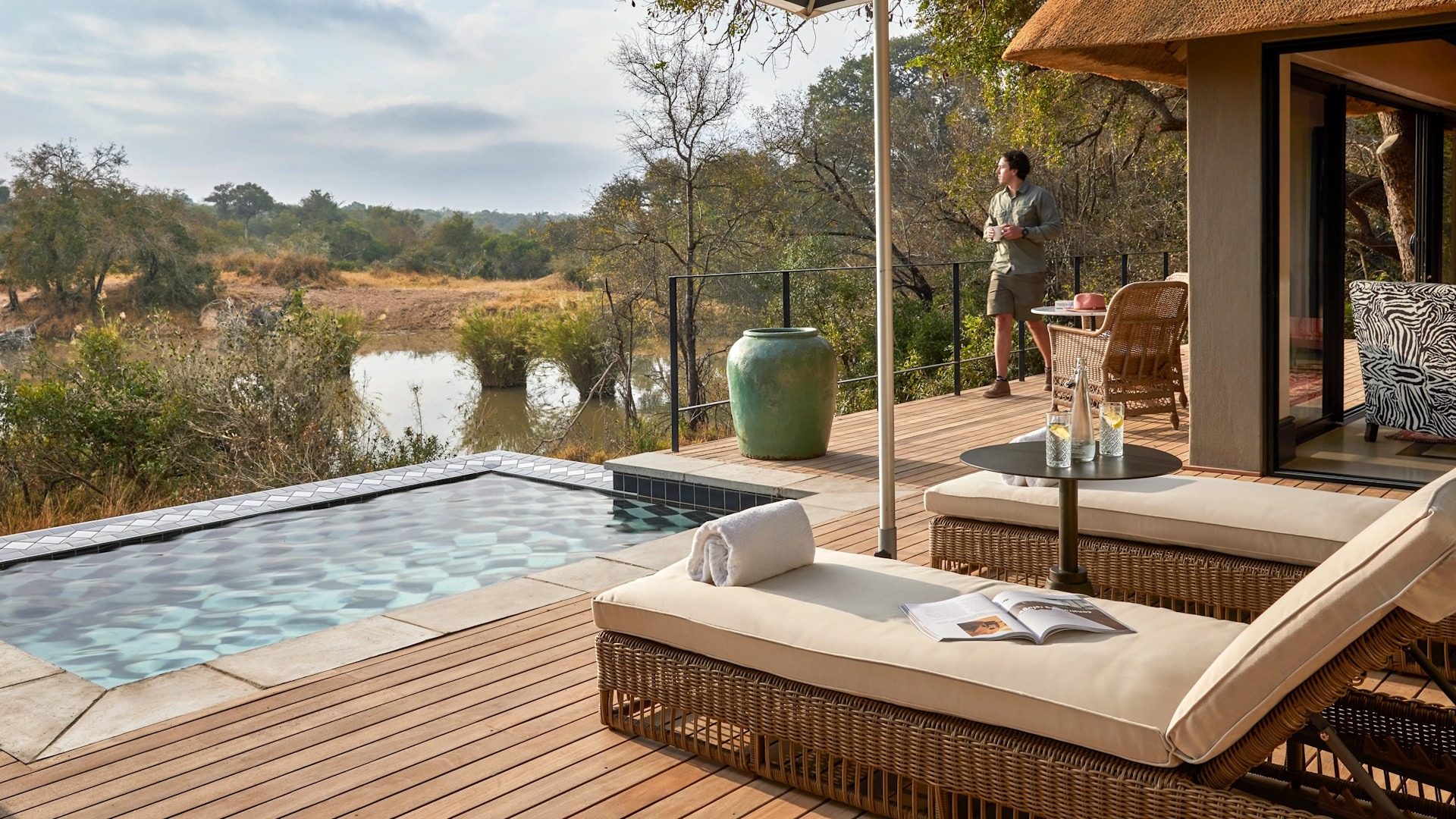A luxury safari lodge suite with private plunge pool and wooden deck overlooking the African bush and a waterhole — the ultimate romantic escape