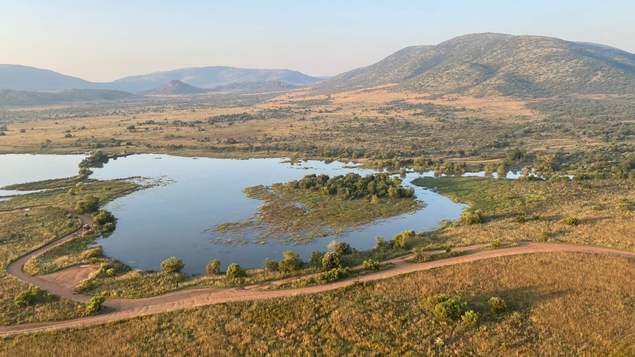 Aerial view of Pilanesberg's volcanic crater landscape with Mankwe Dam shimmering at the centre — the water draws wildlife from across the reserve