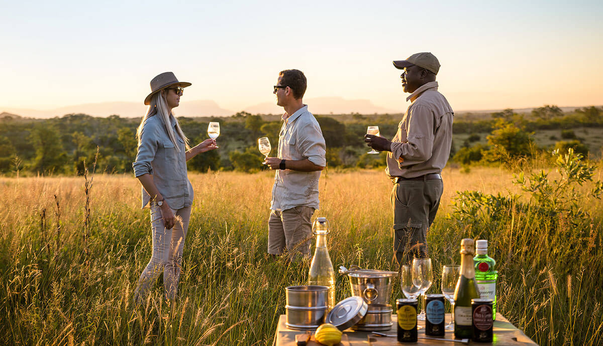 A sundowner moment with a guide in neutral-toned safari clothing — khaki, olive and earth tones are your best friends in the bush