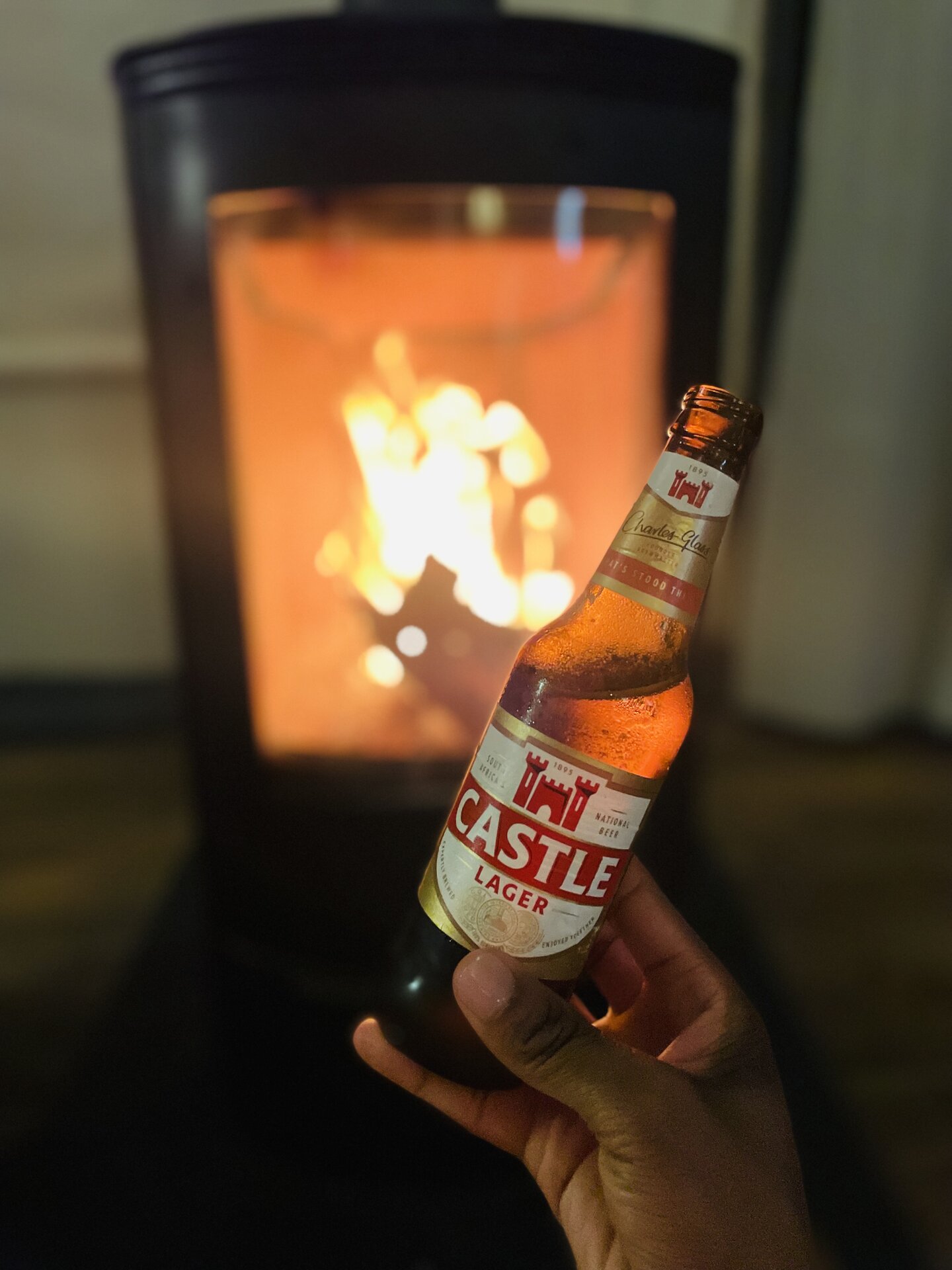 A cold Castle Lager held in front of the glowing wood-burning stove inside the Settlers Drift luxury tent