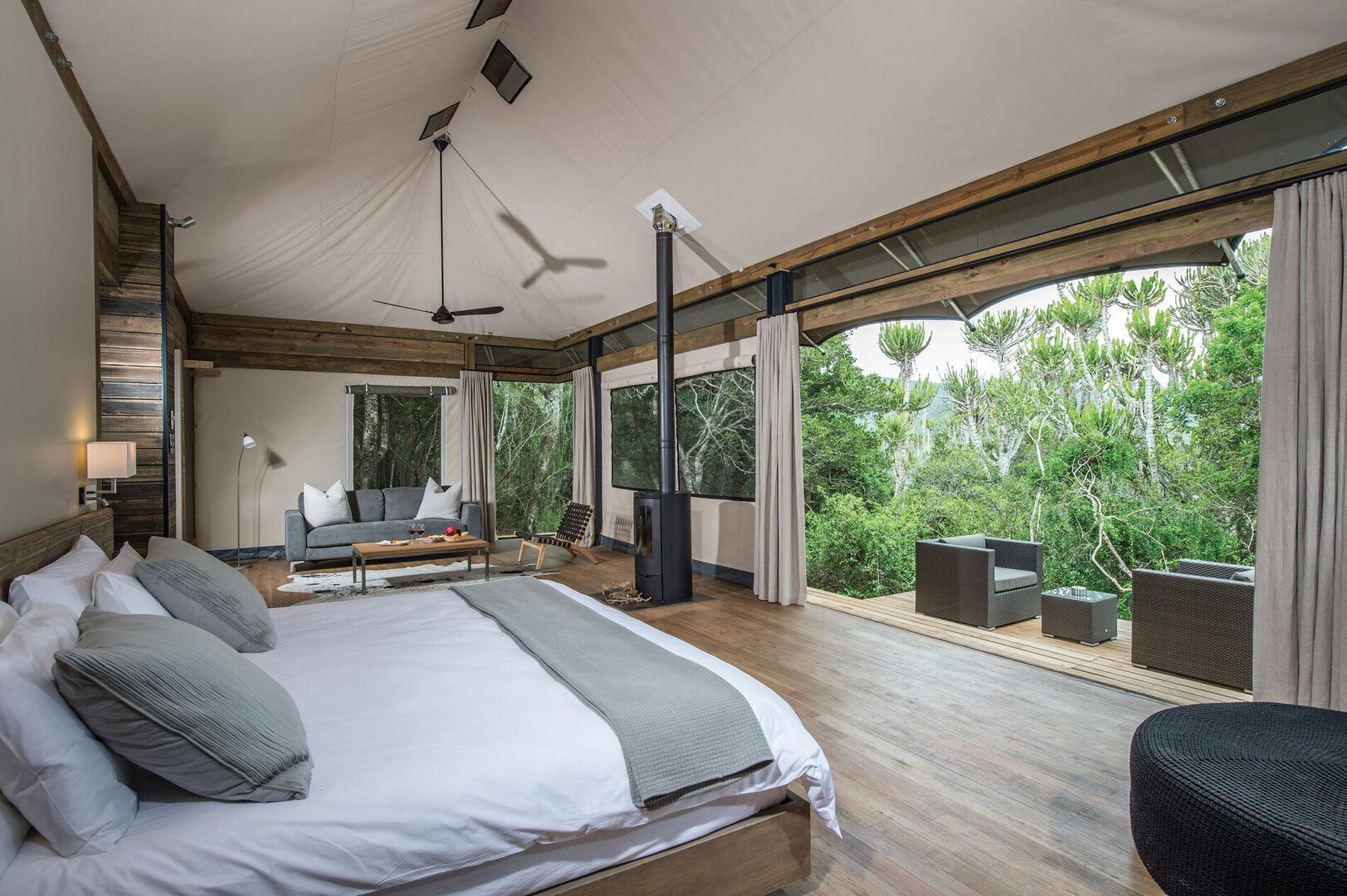 Inside the Settlers Drift luxury tent — a king-size bed dressed in white linen, wood-burning stove, ceiling fan, and canvas walls opening onto the private deck