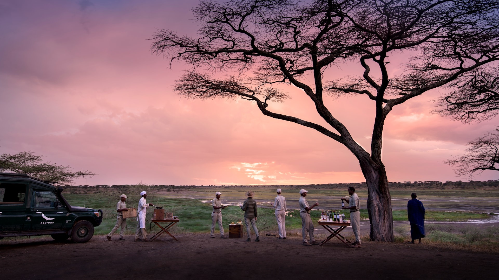 A small group of travellers sharing sundowner drinks at sunset on safari in Africa