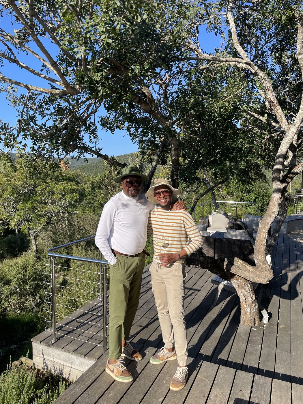 Thabo and Katlego standing together on the wooden deck of their Settlers Drift luxury tent, shaded by a large tree